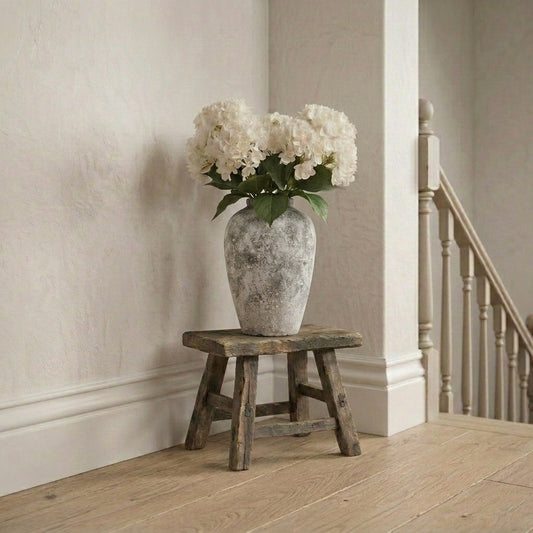 artificial hydrangeas in a textured vase on a wooden stool against a neutral wall on the top of a landing