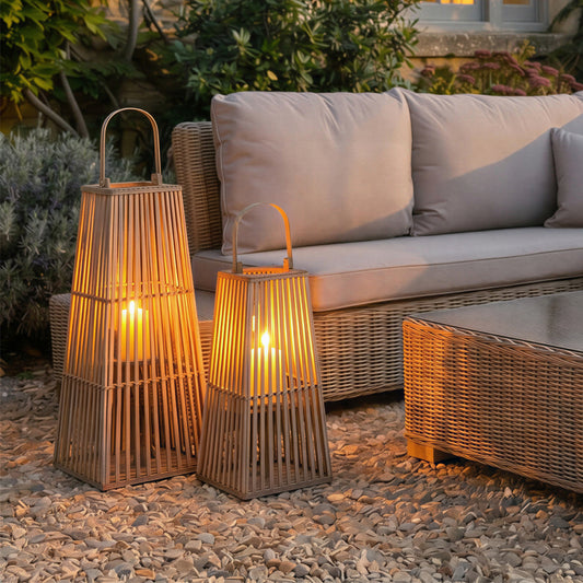 Two wicker lanterns with candles on a stone patio next to a beige outdoor sofa.