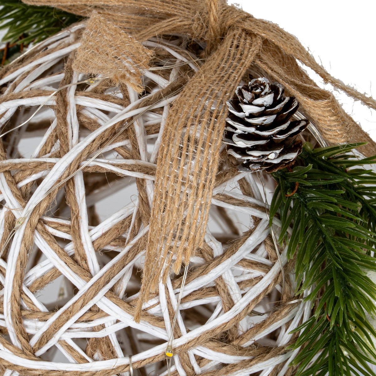 Decorative xmas bauble made of twine with a pine cone and greenery on a white background