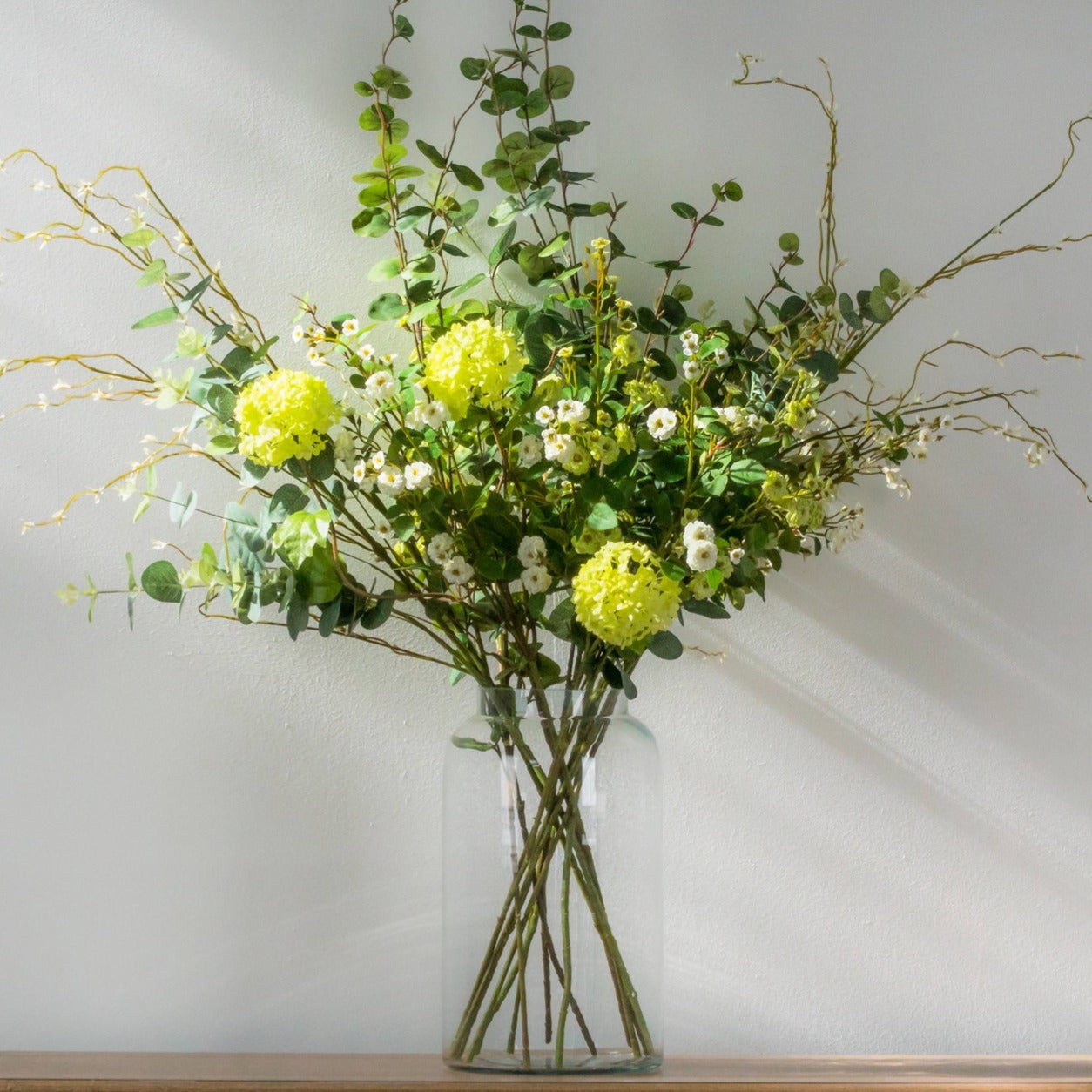Bouquet of green and white flowers in a clear vase on a light background