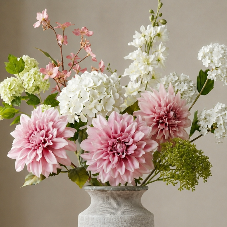 Cottage Garden by Artanna luxury artificial floral arrangement featuring blush pink dahlias, white hydrangeas, delphinium spires and green botanical accents styled in a matte grey stone ceramic vase against a warm neutral backdrop.