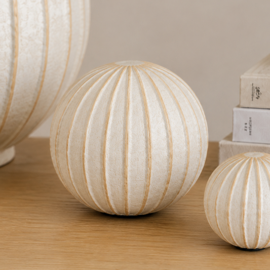 Grove medium cream ribbed decorative ball ornament styled on an oak timber surface alongside a matching large ribbed vessel and smaller ball ornament in a warm neutral interior