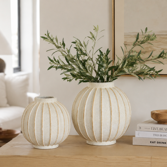 Two round globe decorative vases on a table with faux  greenery in one of them, in a living room setting.