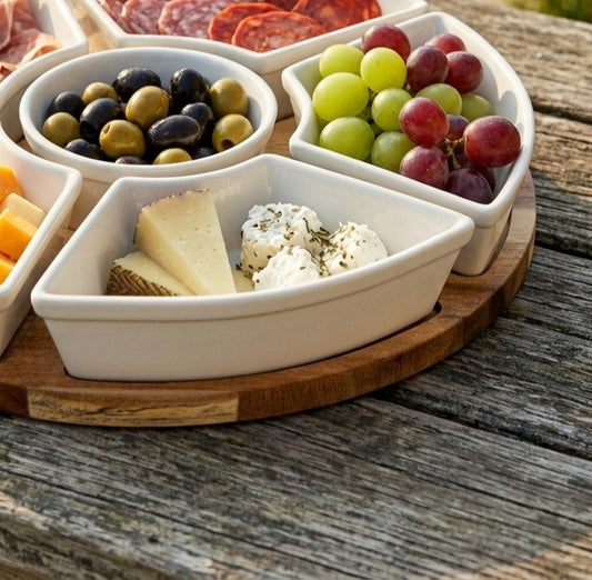 White ceramic platter with sections filled with olives, cheese, and grapes on a wooden surface.