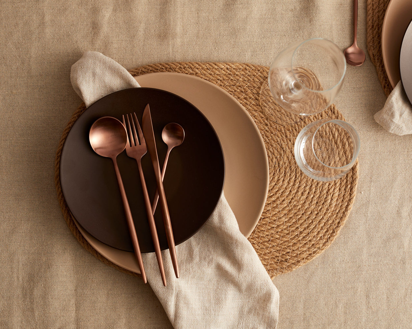 London rose gold cutlery set on dark plate with woven placemat and glasses in an elegant table setting