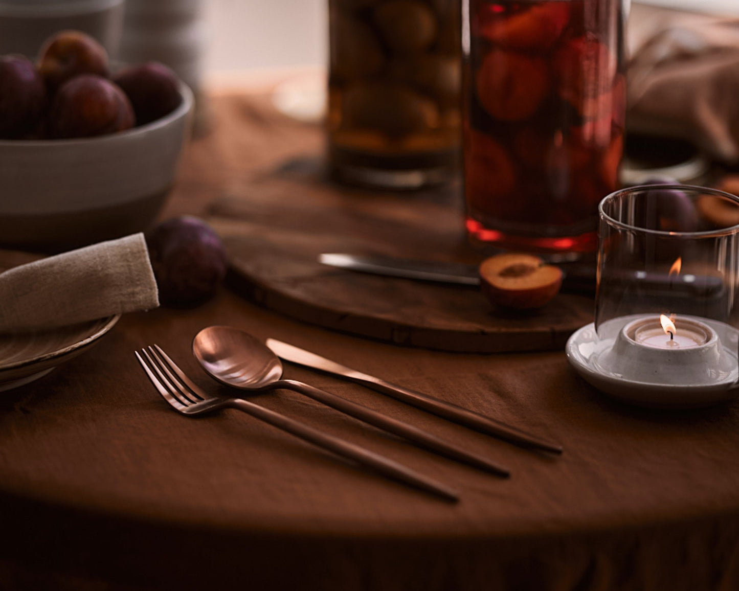 London rose gold cutlery set in an elegant dinner table setting with candles on a wooden surface