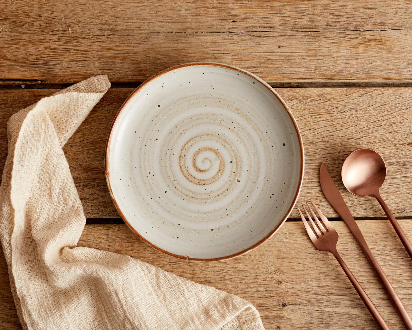London rose gold cutlery set styled on wooden dining table with ceramic plate and linen napkin