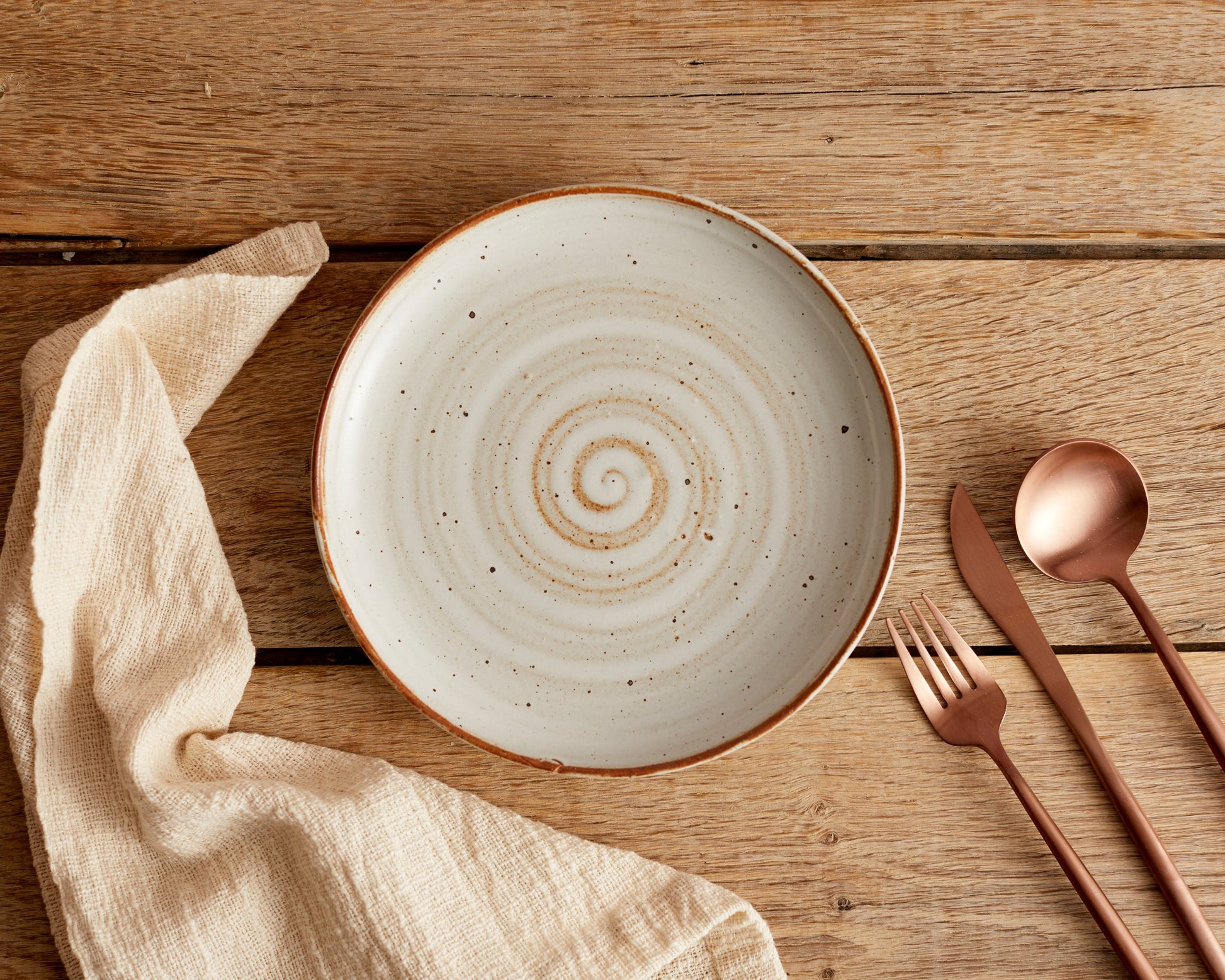 London rose gold cutlery set styled on wooden dining table with ceramic plate and linen napkin