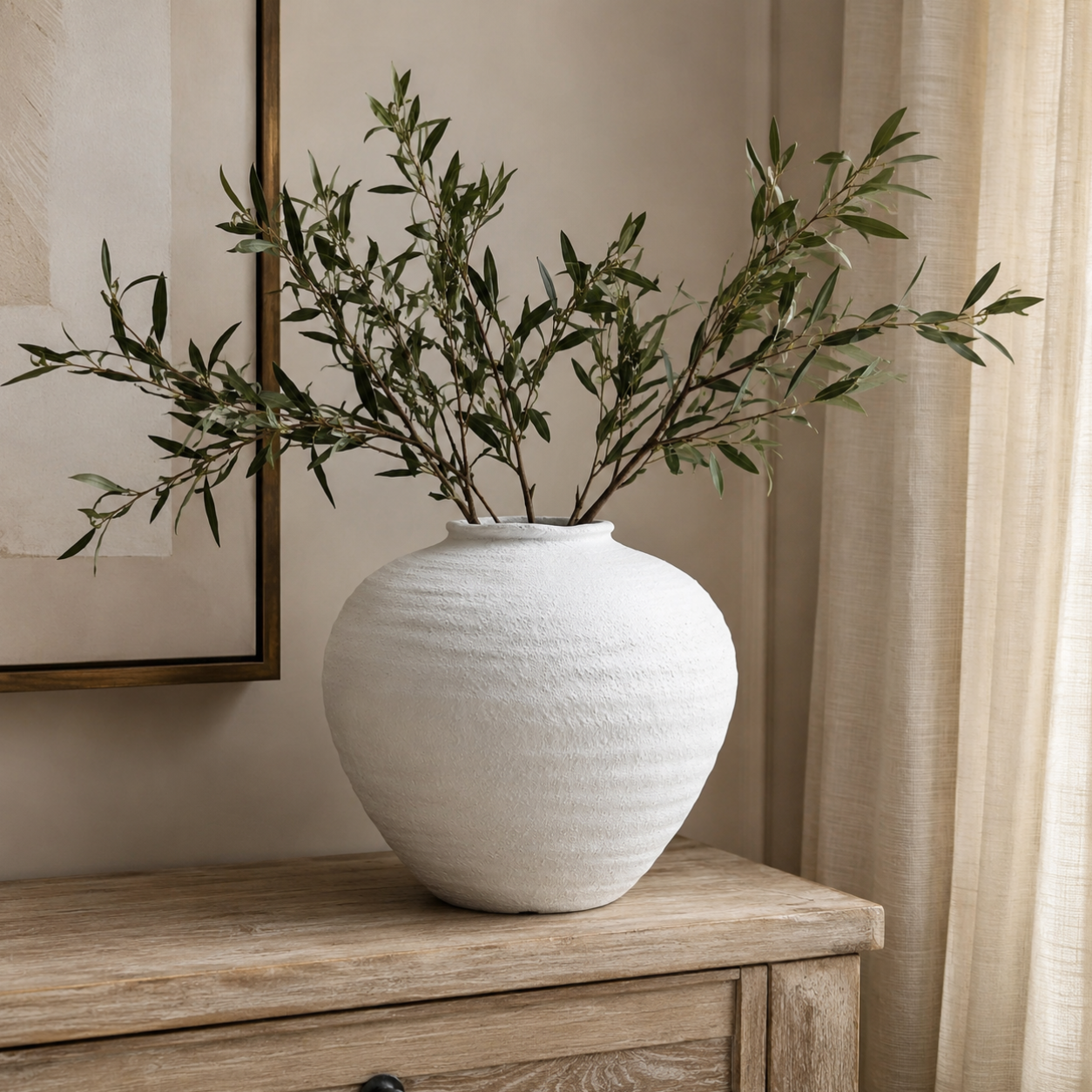 White textured vase with green artificial olive branches on a wooden surface, with a neutral background