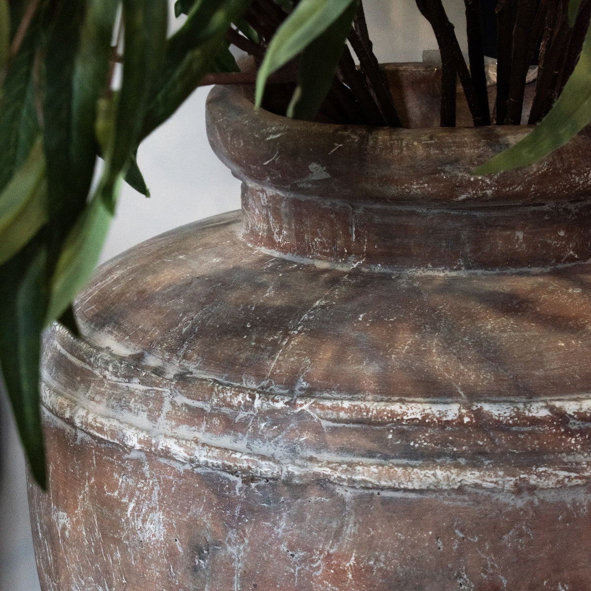 Close-up of an old, textured brown pot with plants inside against a neutral background