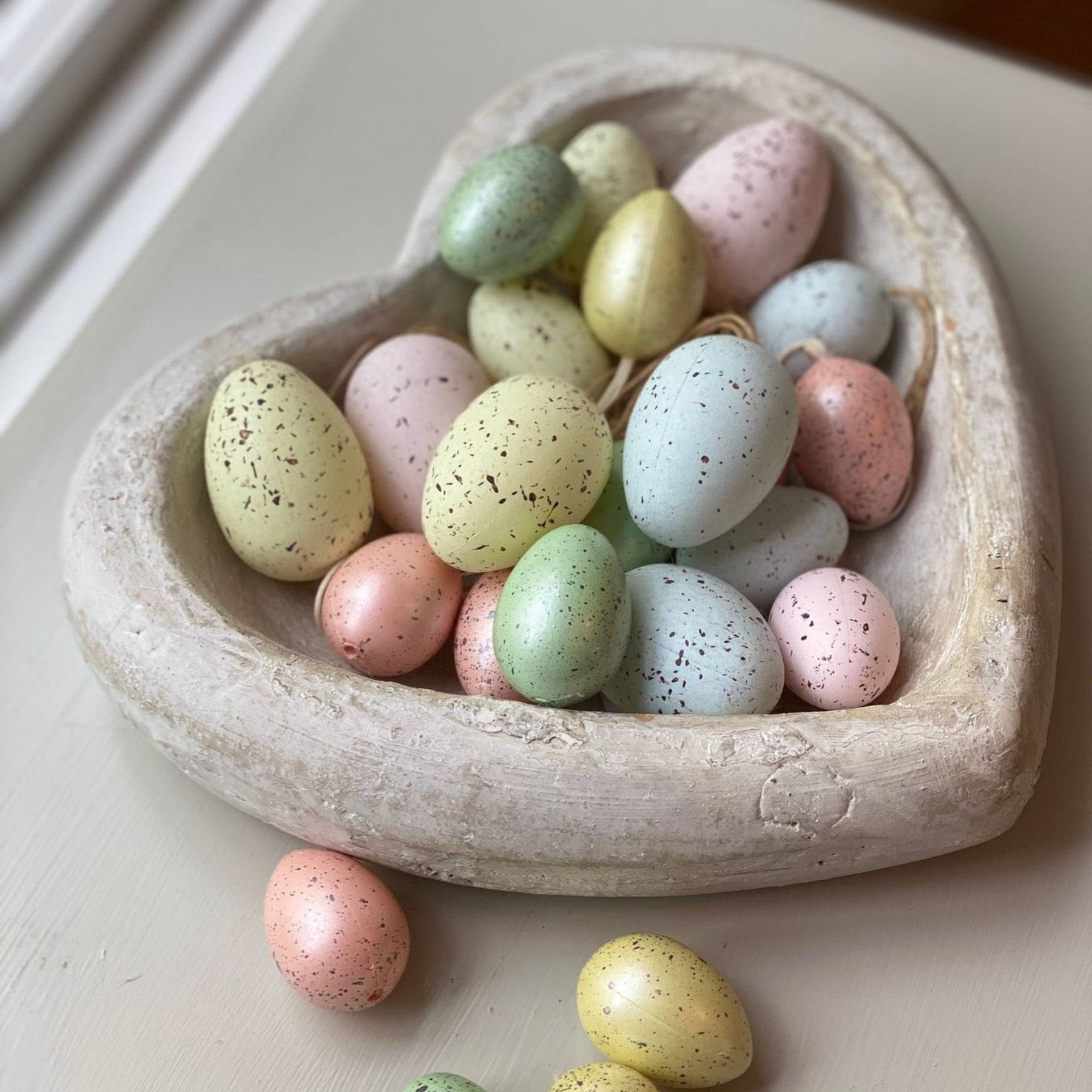 Heart-shaped stone decorative bowl filled with pastel speckled Easter eggs on a light surface.