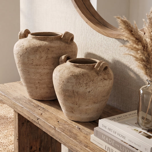 Two rustic urh vase pots on a rustic console table with books and a vase in the background.