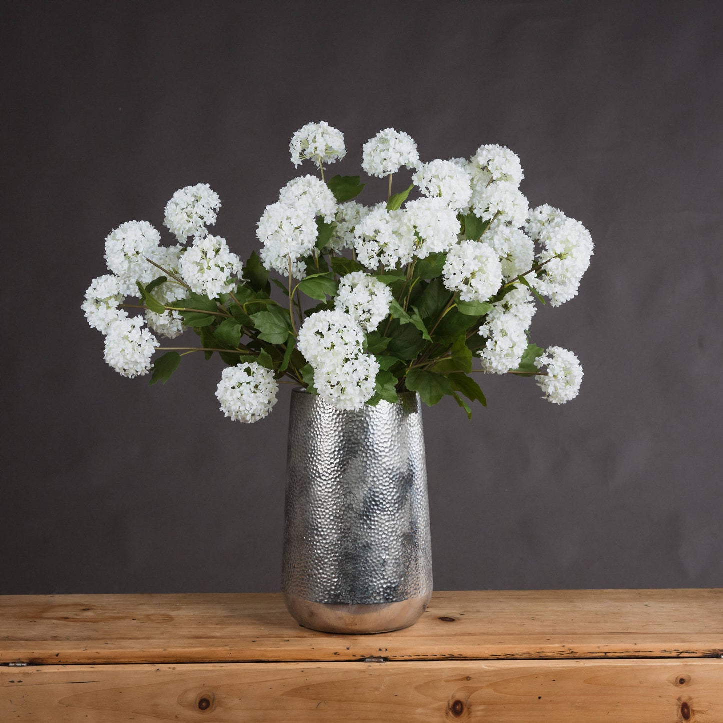 Silver vase with white flowers on a wooden surface against a dark background