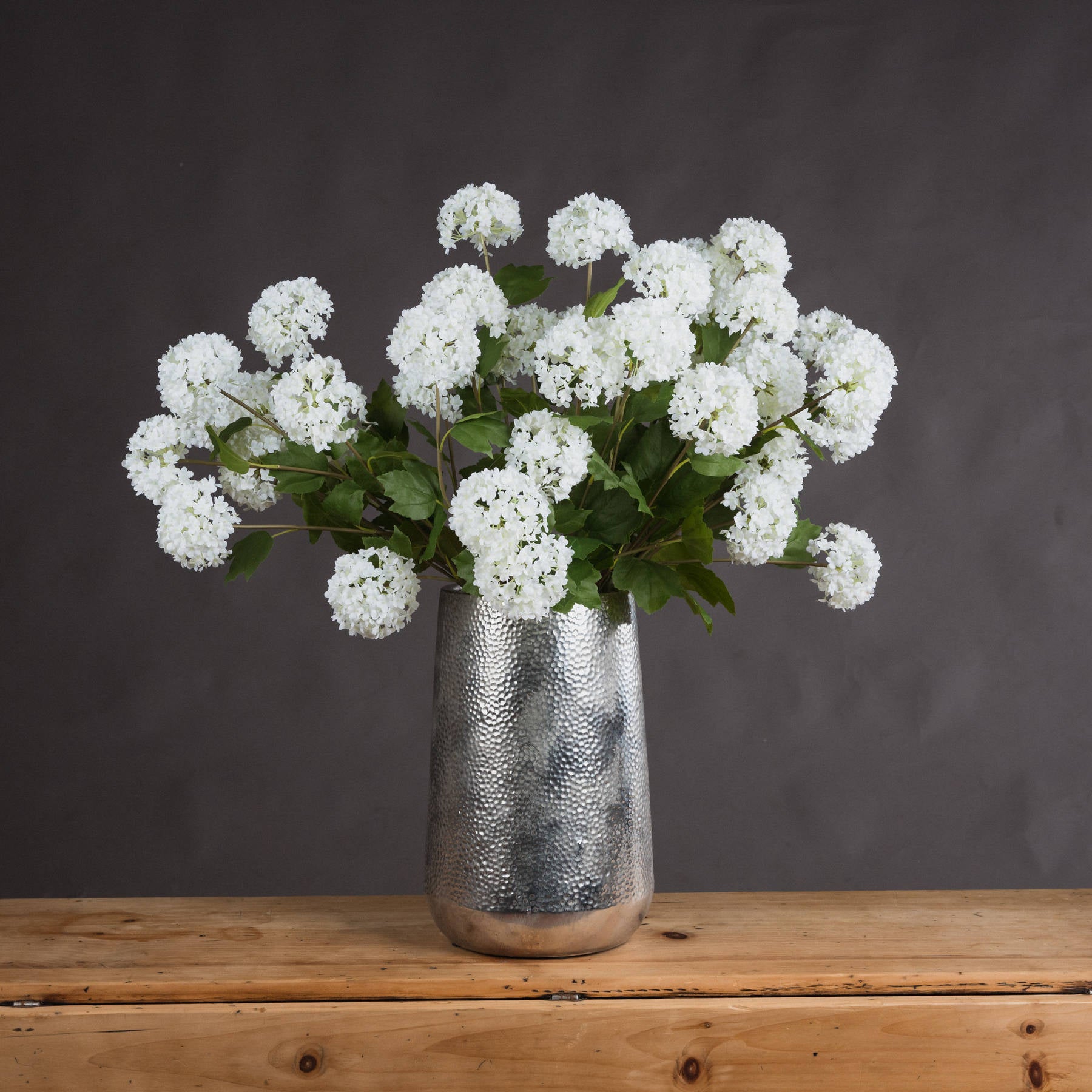Silver vase with white flowers on a wooden surface against a dark background